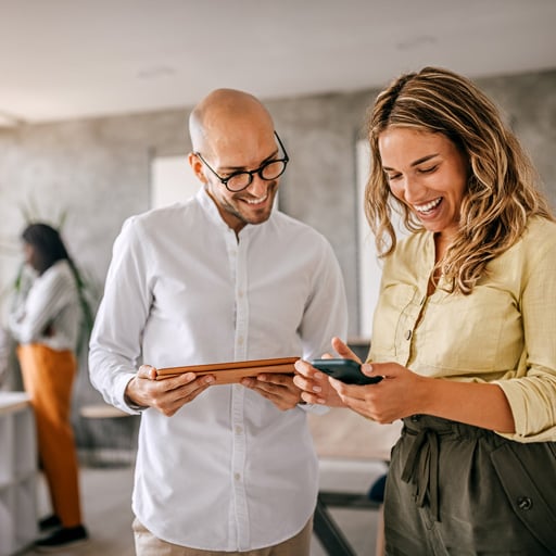 A woman shows her smartphone to a colleague while discussing mobile credentials, highlighting secure and seamless access to workplaces using digital employee badges.